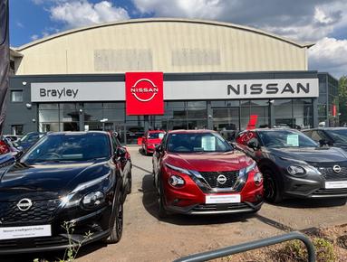 Nissan dealership with multiple cars parked in front, including black and red models.