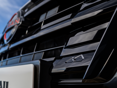 Close-up of a black car grille with a manufacturer's badge and a camera symbol.