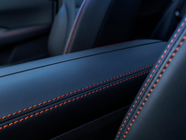 Close-up of car seat with black leather and orange stitching detail.