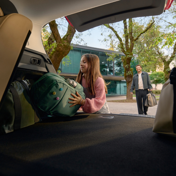Girl placing a backpack into a car boot, man walking towards the car in the background.