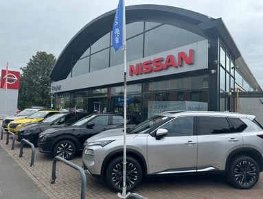 Nissan dealership with multiple cars parked in front of glass-fronted showroom.