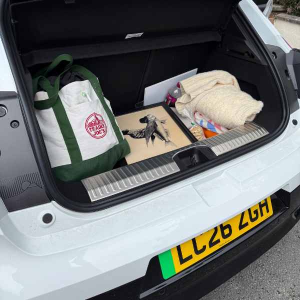 Open car boot with tote bag, blanket, artwork, and laptop.