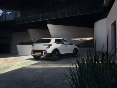 White SUV parked on a concrete surface near modern architectural elements, viewed from the rear.
