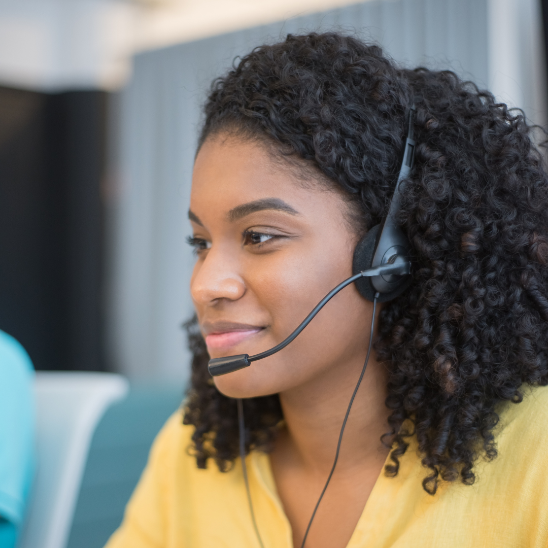A person with curly hair wearing a headset and a yellow top.