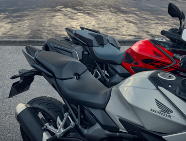 Two Honda motorcycles parked side by side, one grey and one red, viewed from behind.