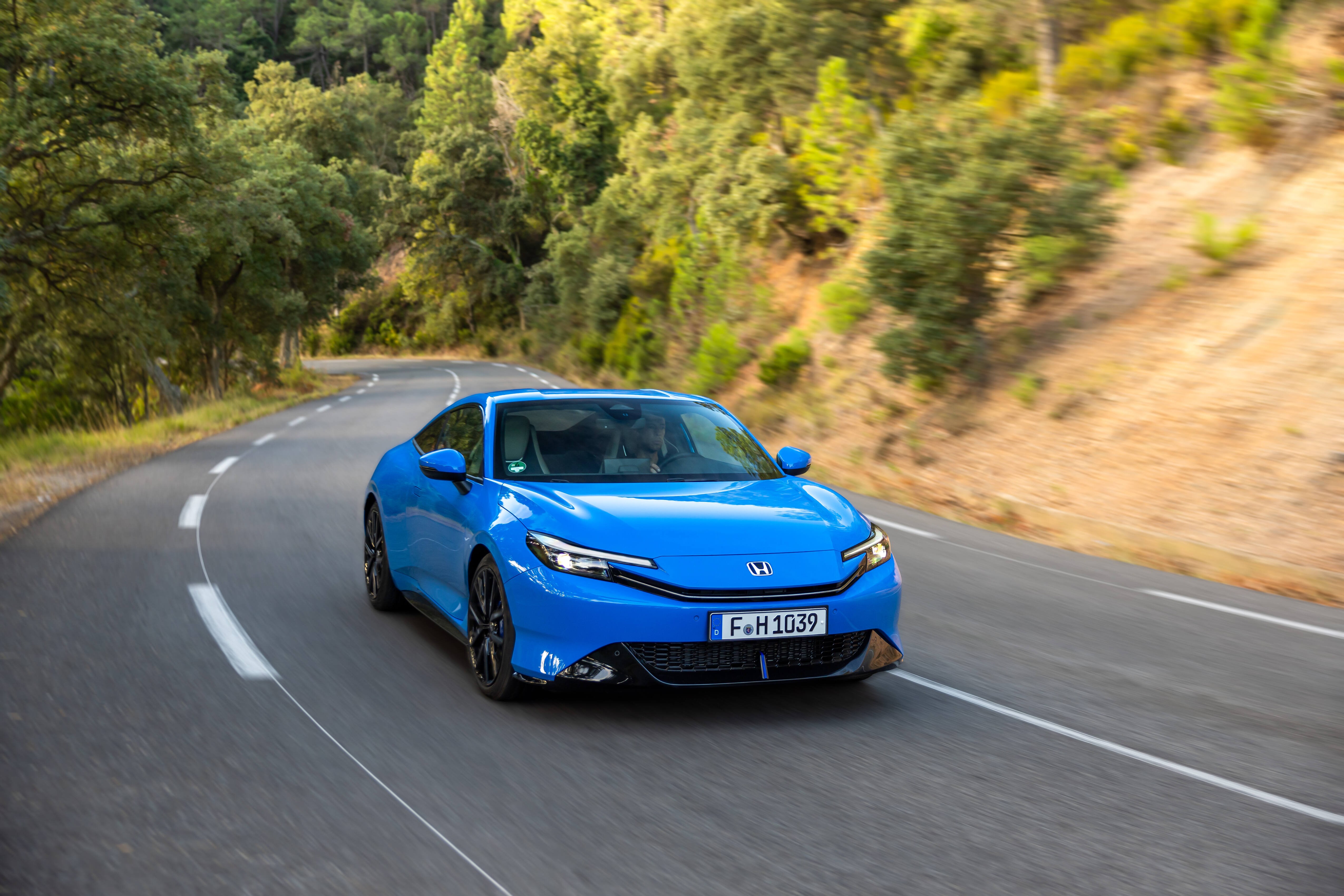 Blue car driving on a winding road surrounded by trees.