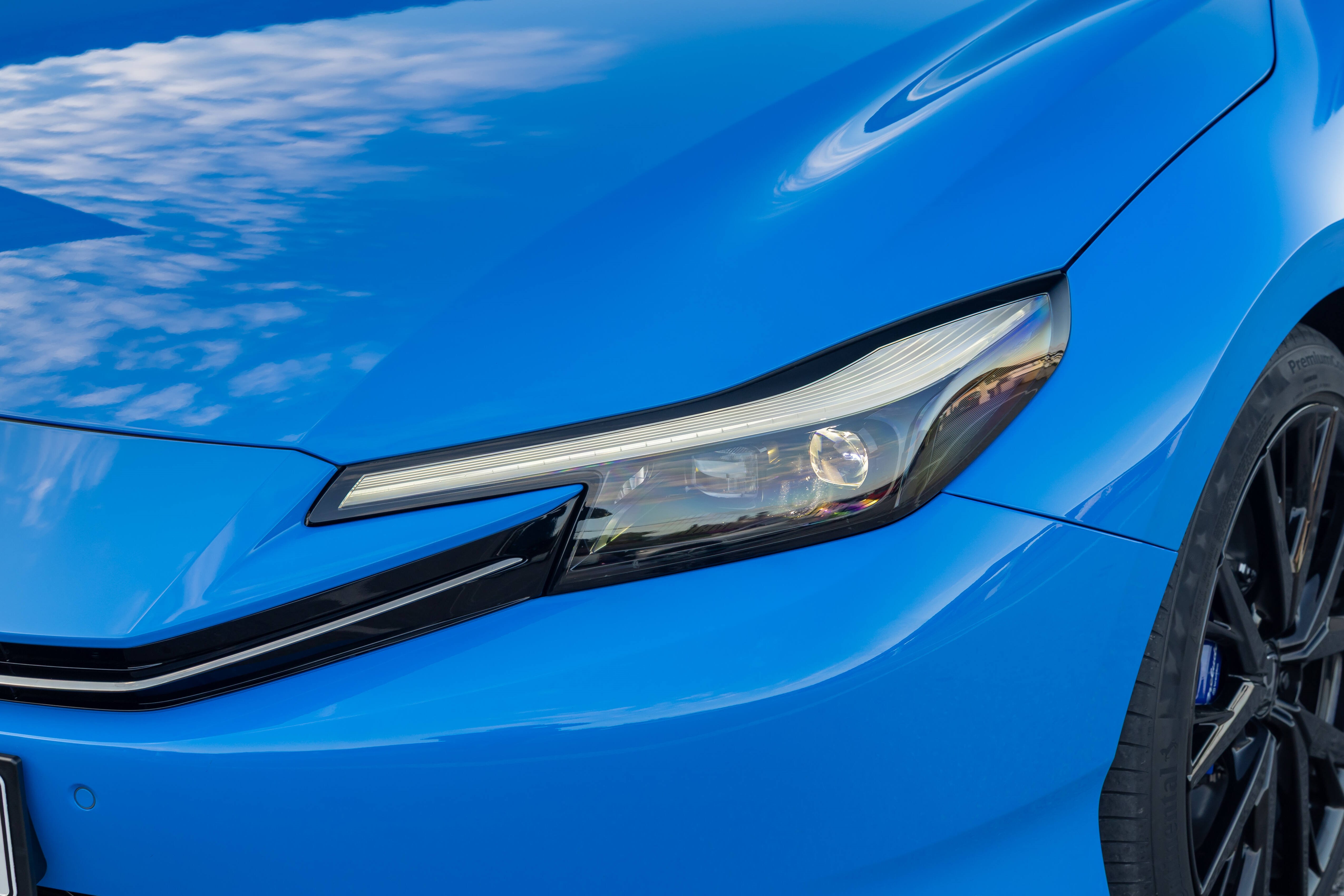 Close-up of a blue car's front headlight and tyre.