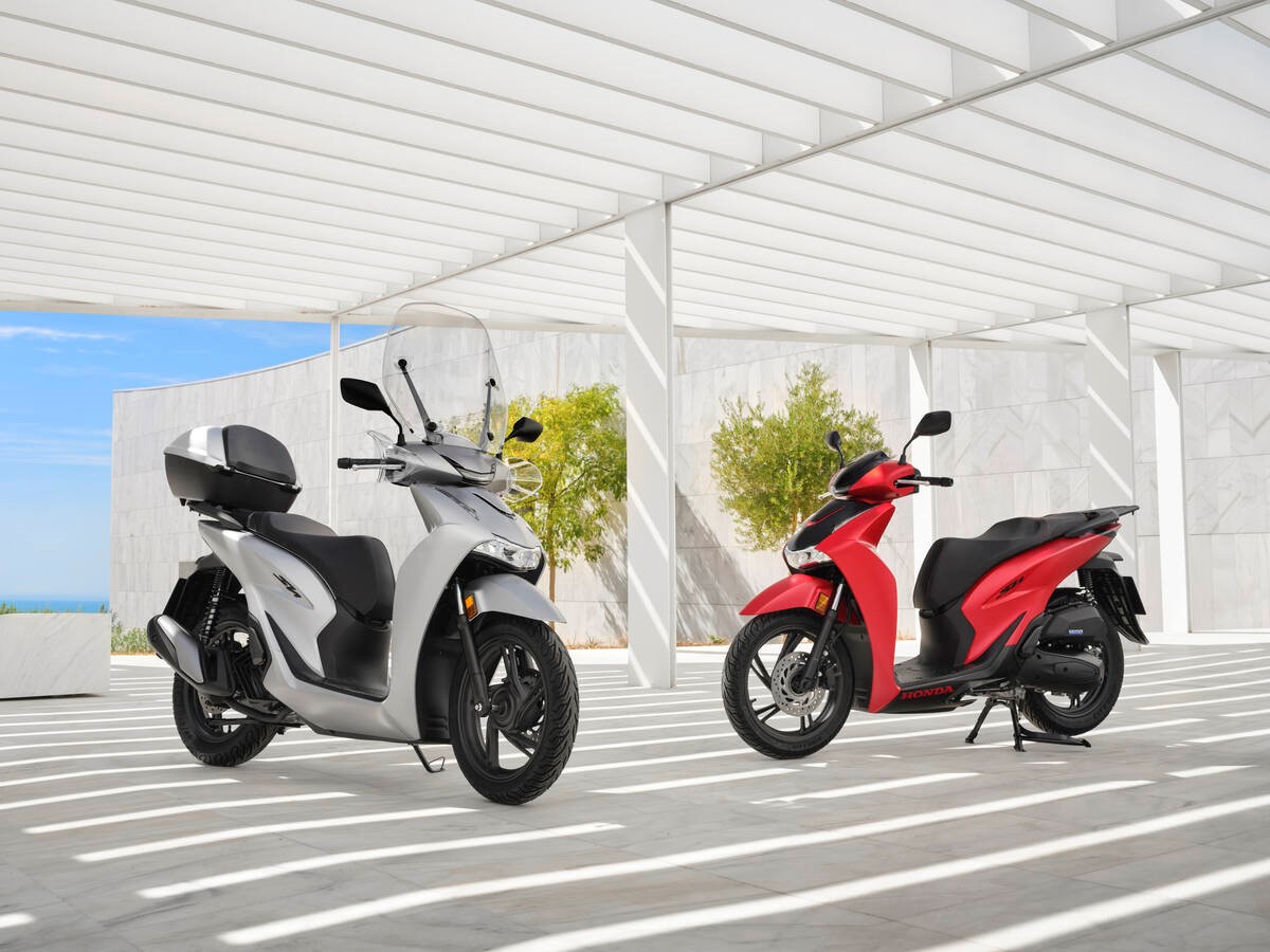 Two scooters, one silver with a windshield and one red, parked side by side.
