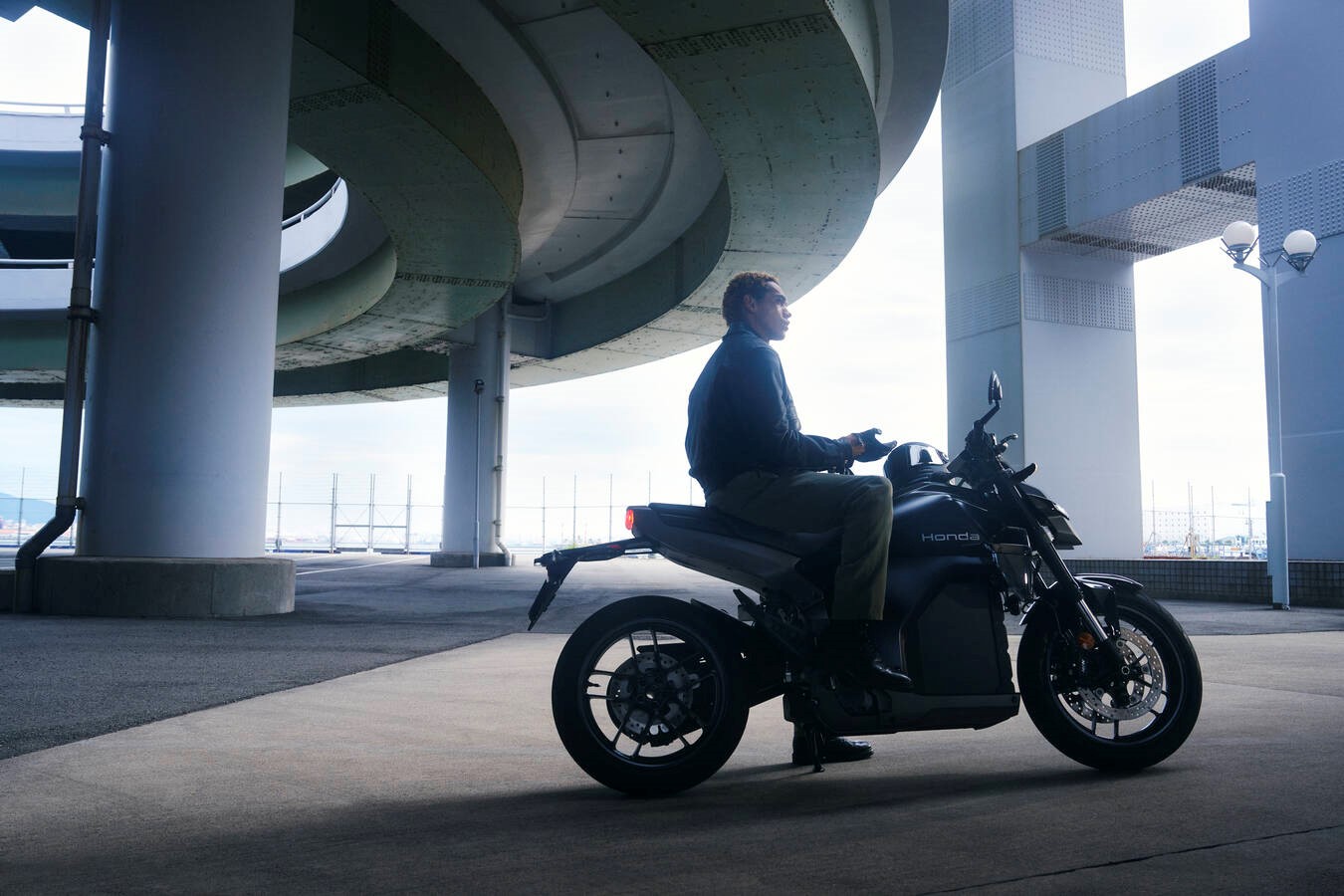 Person sitting on a parked Honda motorcycle under a large concrete structure.