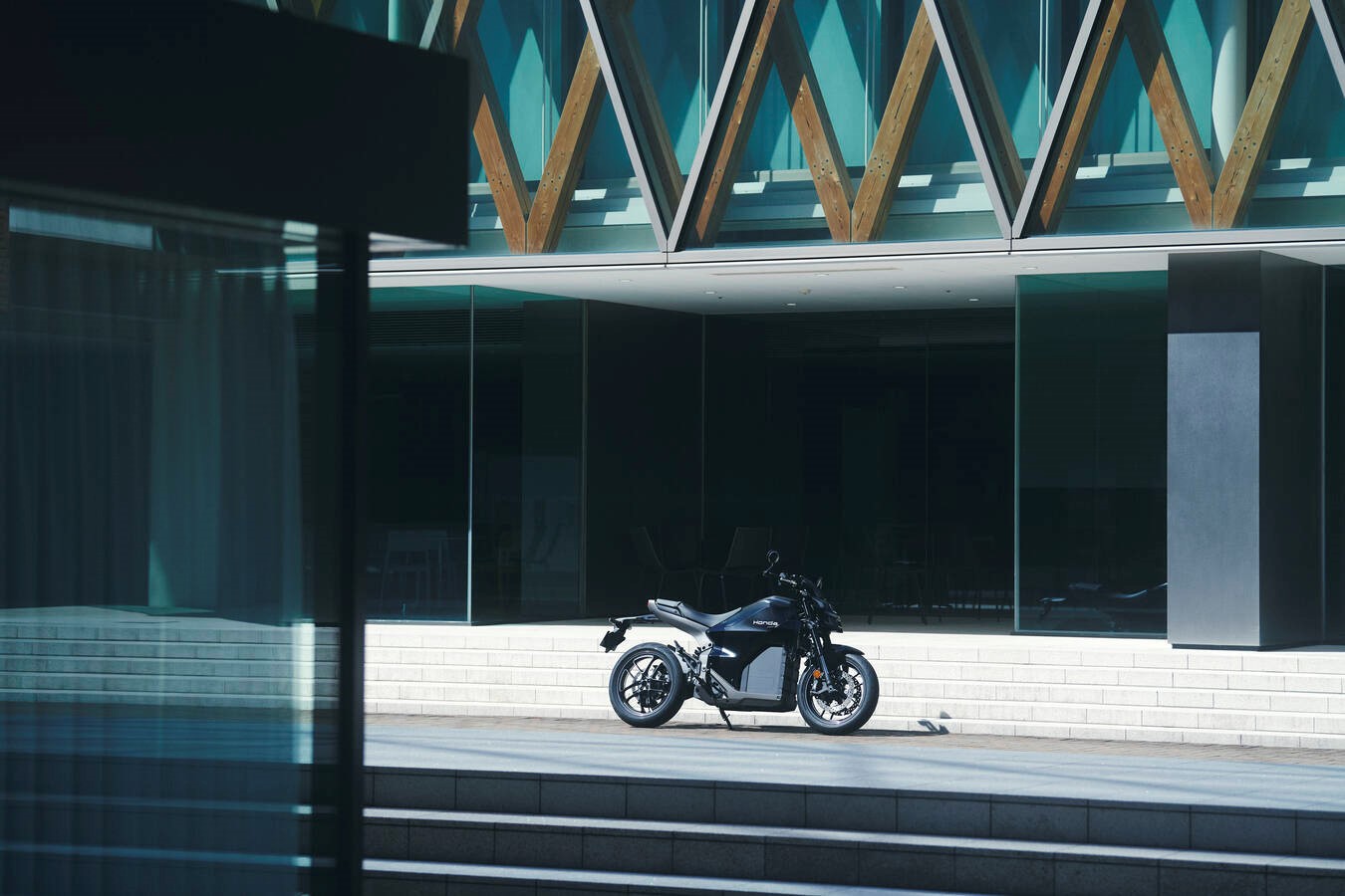 Black motorcycle parked in front of a modern building with glass and wood accents.