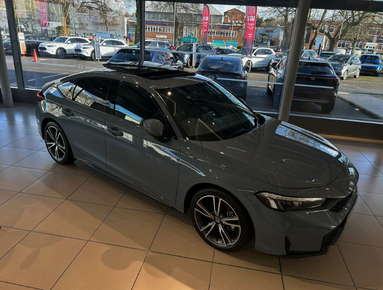 Grey saloon car displayed indoors with large windows.