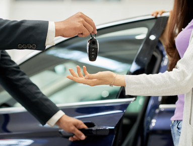 Person handing car key to another person near a vehicle.