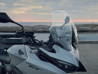 Alt: Close-up of a Honda motorcycle's front with windshield and handlebars.