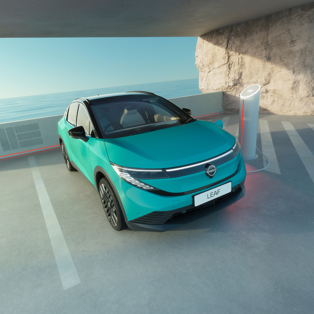 A teal electric car parked beside a charging station next to a cliff.