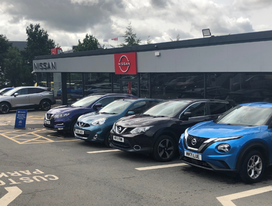 Line of Nissan cars parked in front of a dealership.