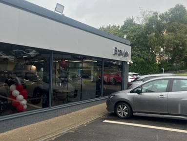 Car parked outside a dealership with balloons inside the showroom.