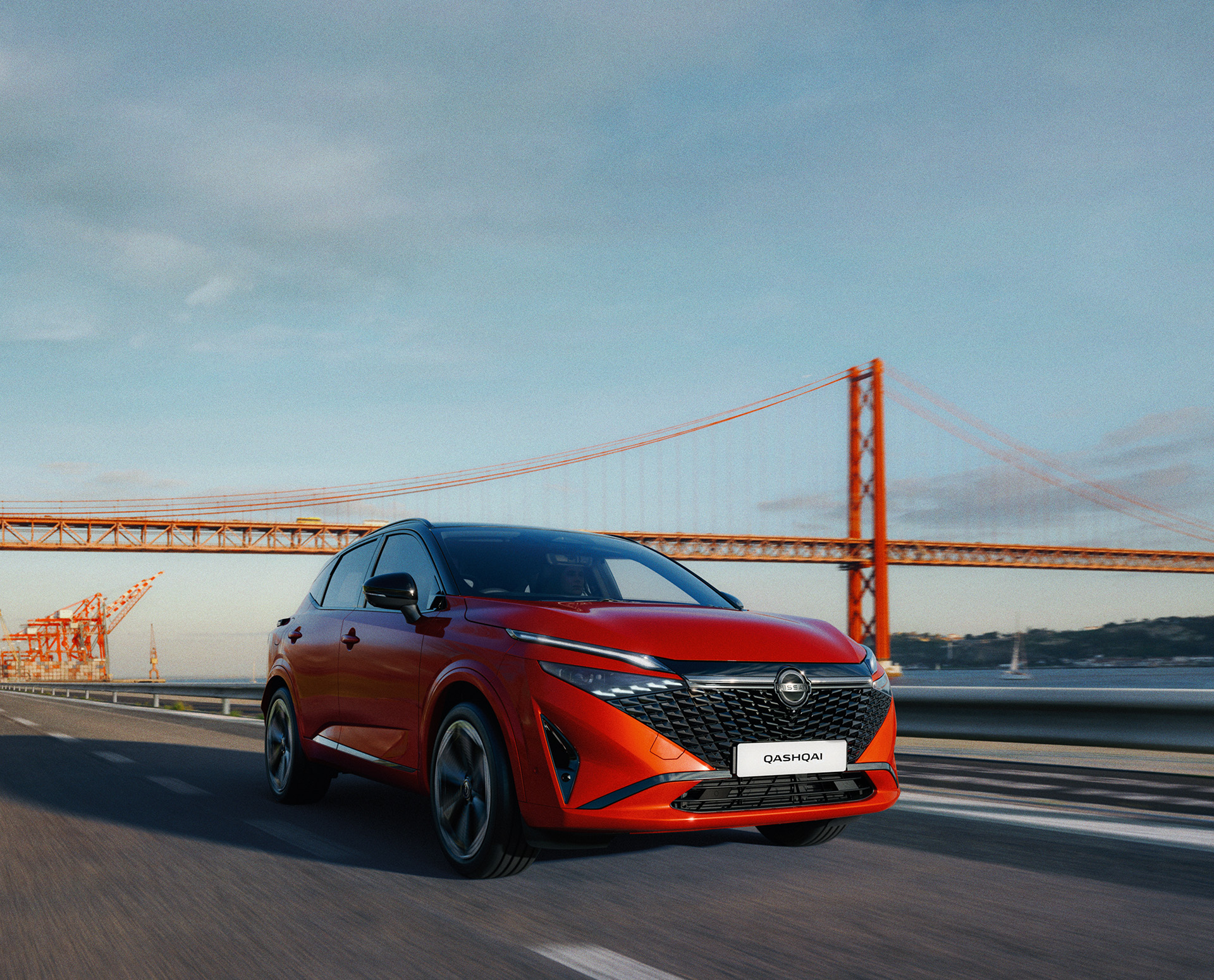 Red SUV driving on a road with a large suspension bridge in the background.