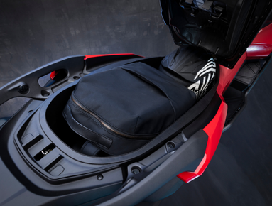 Open scooter seat storage containing a bag and a helmet.