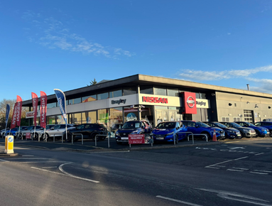 Car dealership with multiple vehicles and flags outside.