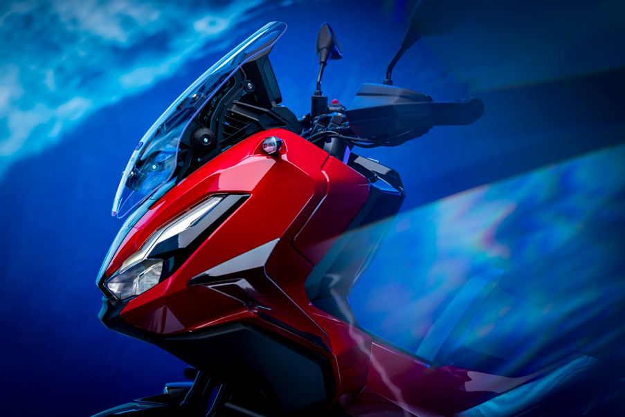 Red motorcycle with windscreen and handlebars viewed from the front right angle.