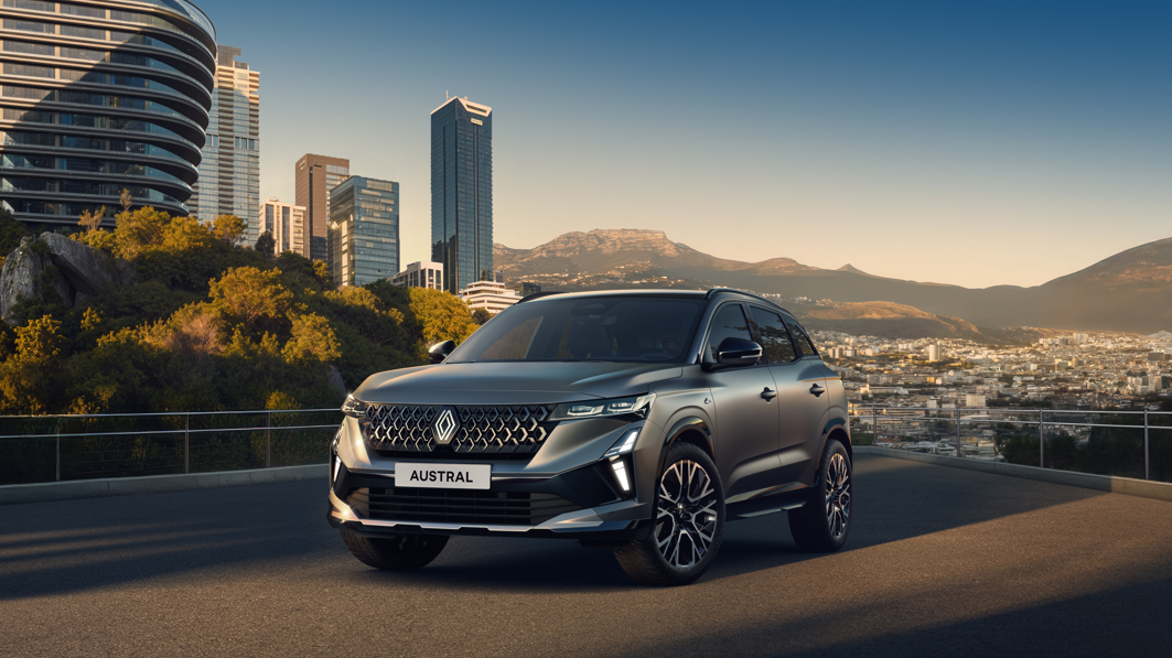 SUV with 'Austral' plate on a city road with buildings and mountains in background.