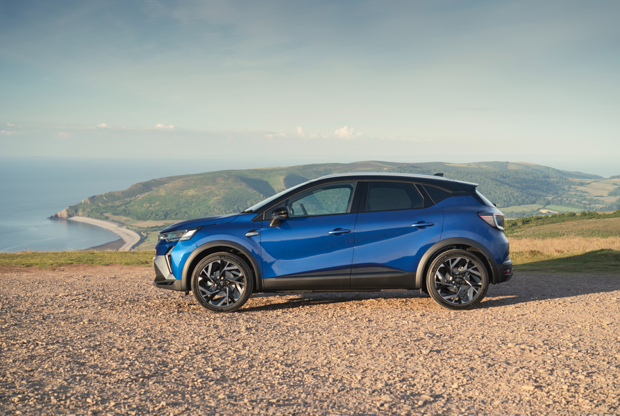 Blue SUV parked on a gravel path with hills and coastline in the background.