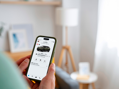Person holding phone displaying car information in an app.