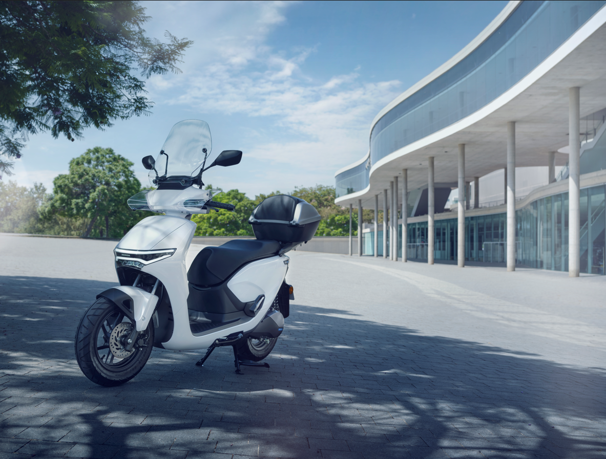 White electric scooter with a windshield parked near a modern building.