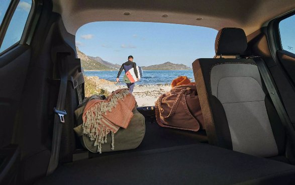 View from car boot with bags and person holding surfboard.
