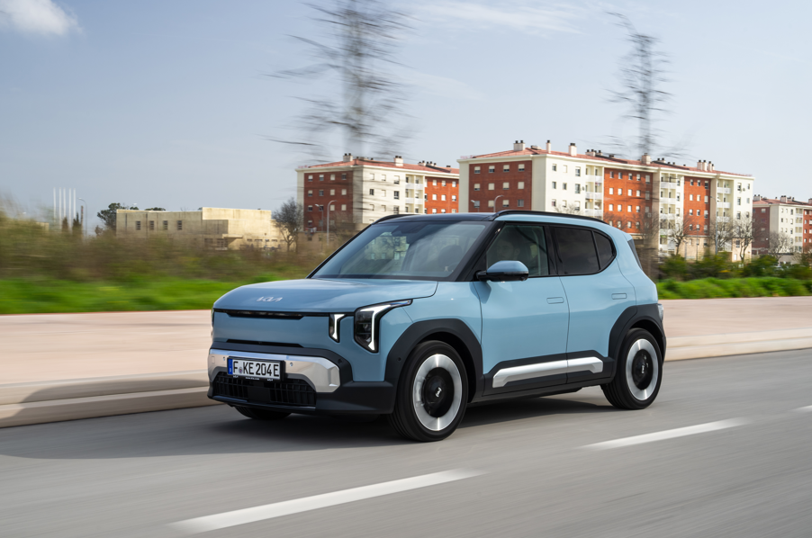 A blue SUV driving on a road beside residential buildings.