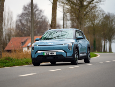 Blue SUV driving on a country road with trees in the background.