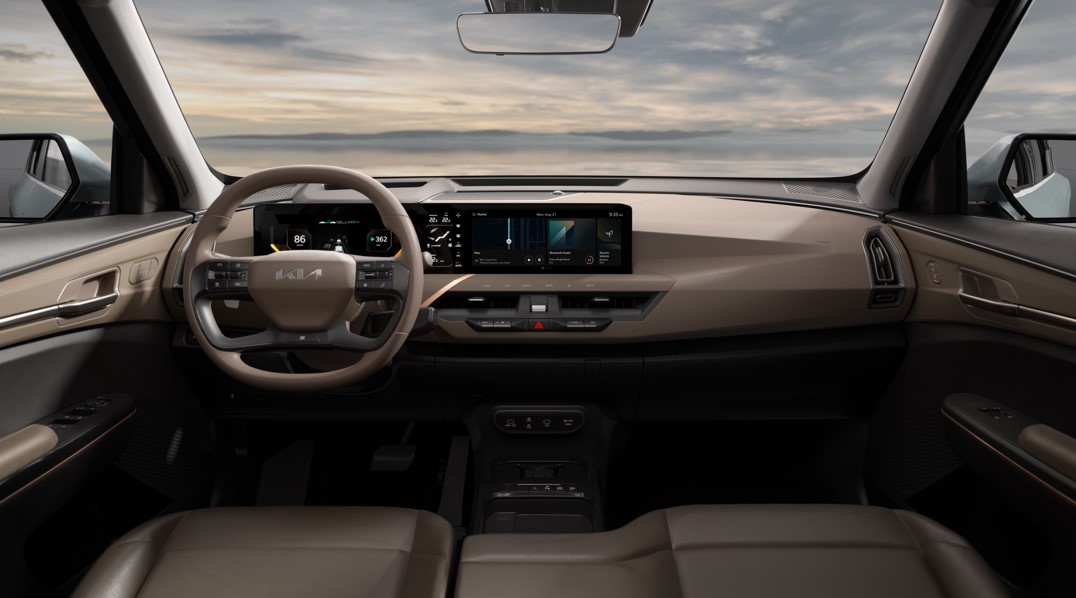 Car dashboard with digital display and tan interior, viewed from the back seat.
