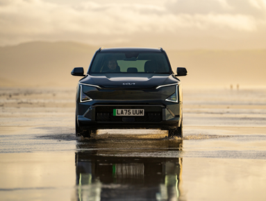 Front view of a dark SUV driving on wet sandy terrain.