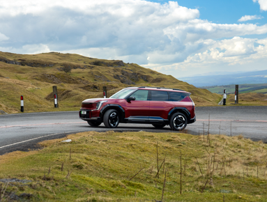 Red SUV driving on a winding road in a hilly landscape.