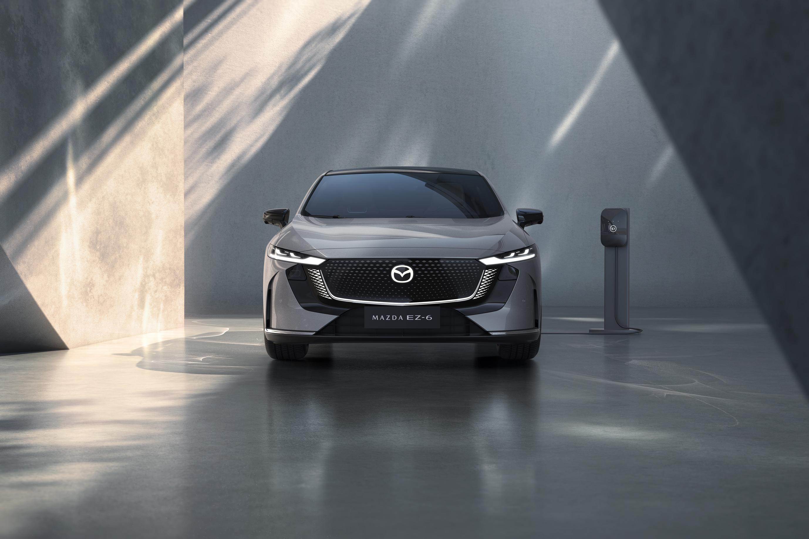 Front view of a grey car with Mazda badge, parked near a charging station.