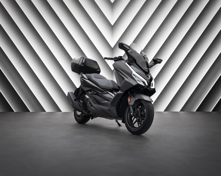 Black modern motorbike with a large windscreen and storage box, parked indoors.