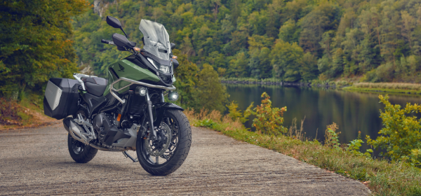 Green Honda NC750X standing upright Infront of a forested body of water