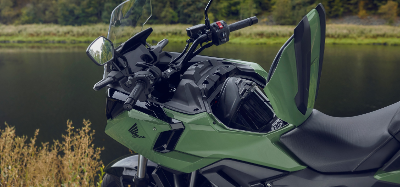 Green motorcycle with open storage compartment near a river.