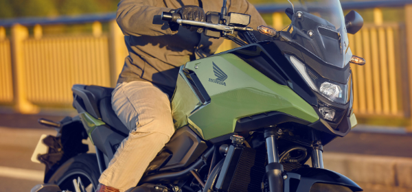 Motorcyclist riding a green Honda NC750X on a road wearing gloves