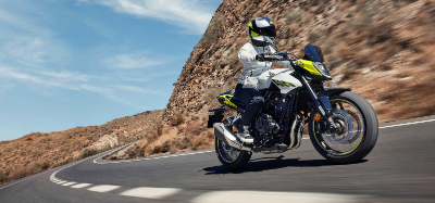 Motorcyclist in white jacket riding a motorcycle on a curved road next to a rocky hillside.
