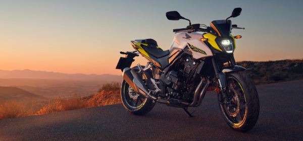 A white and yellow Honda motorcycle parked on a road during sunset.