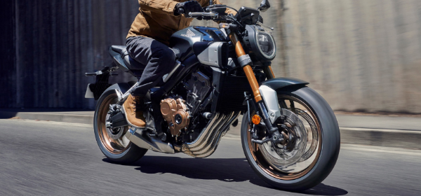 Motorcyclist in a brown jacket riding a black and silver motorbike on the road.
