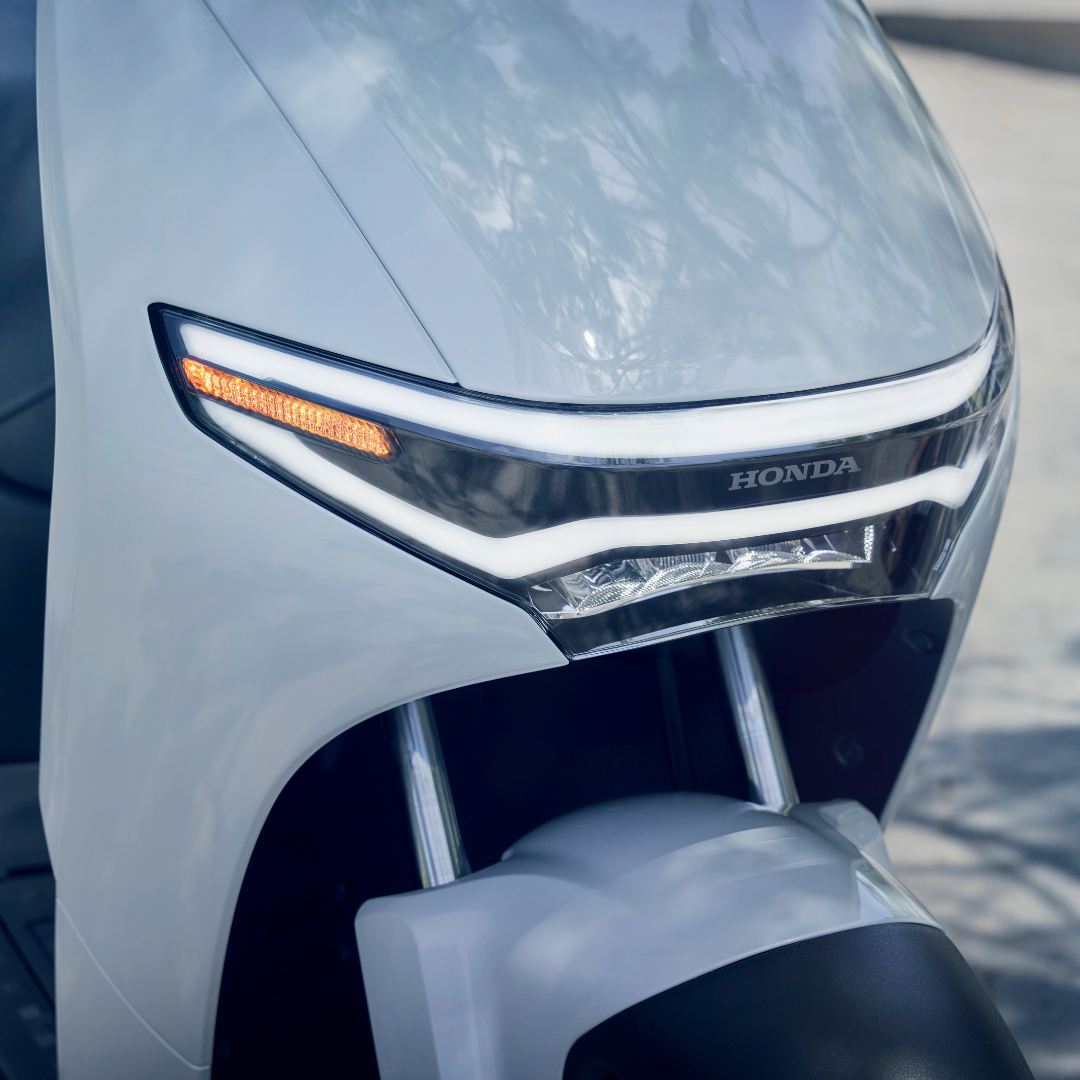 Close-up of a Honda scooter's front, showcasing the headlight and brand logo.