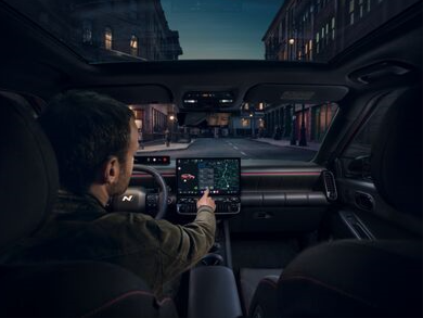 Driver using touchscreen in a car with a panoramic sunroof at night.