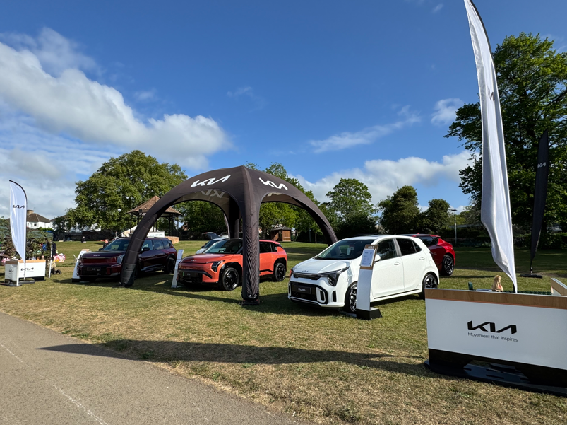 Four cars displayed under a branded canopy with flags and signage in an outdoor setting.