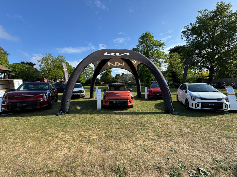 Five Kia cars displayed under a black canopy on grass.