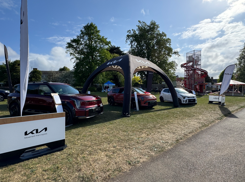 Kia cars displayed under branded canopy with signage at an outdoor event.