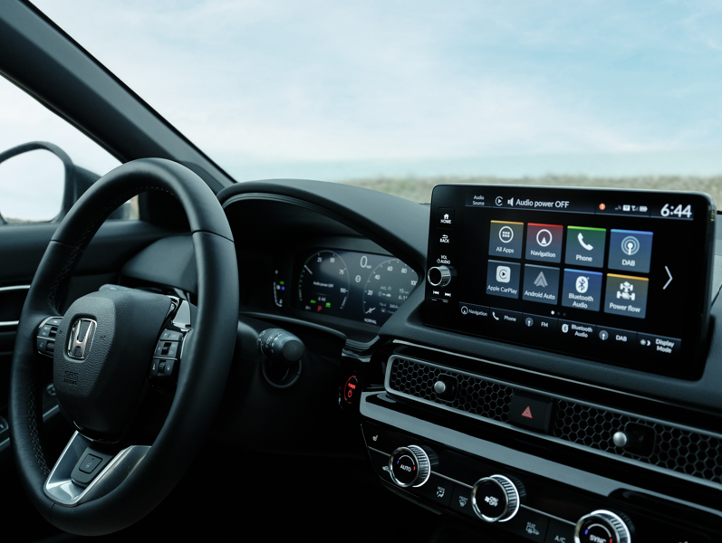 Car dashboard with steering wheel and touchscreen display showing various app icons.