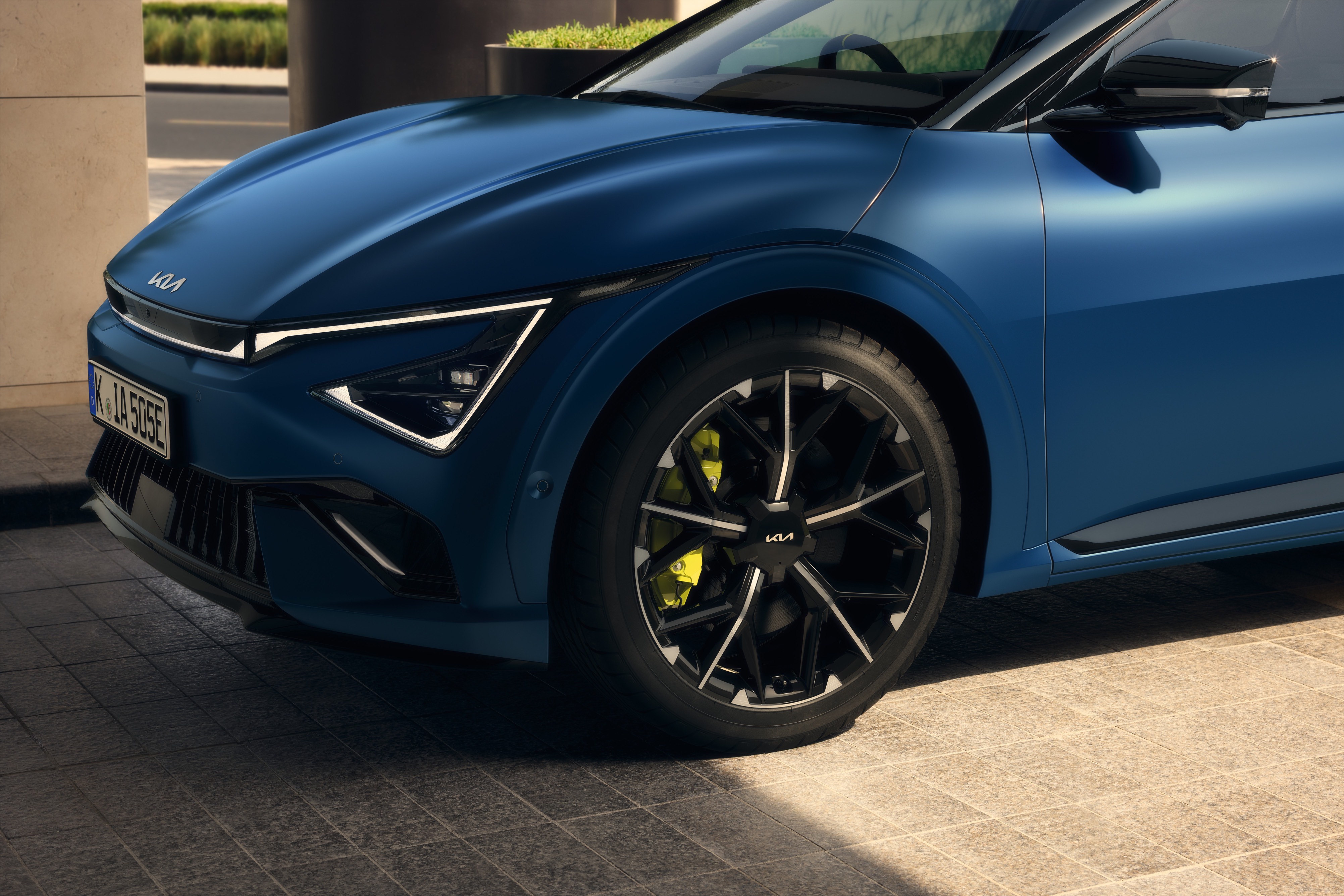 Close-up of a blue car's front left wheel and headlight.
