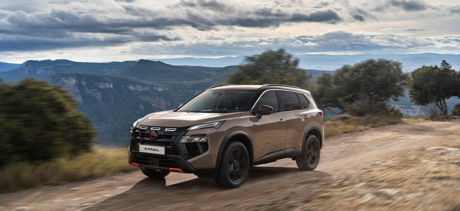 Bronze SUV driving on a dirt road with hills and trees in the background.